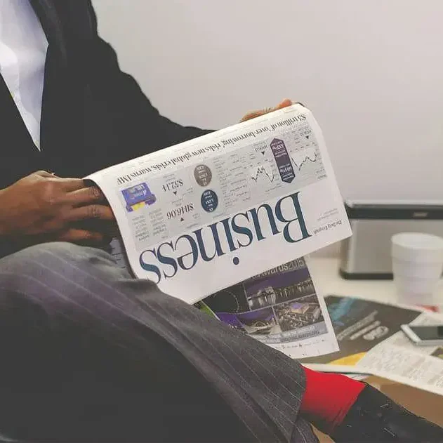 Ein Mann in einem Anzug liest eine Zeitung im Wartezimmer. Rote Socken sind sichtbar.