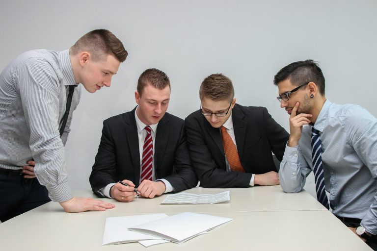 Vier Männer in Anzügen besprechen Dokumente am Tisch.