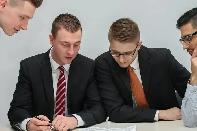 Vier Männer in Anzügen besprechen Dokumente am Tisch.