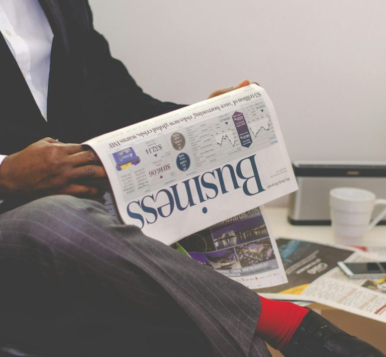 Mann in Anzug hält eine Zeitung mit dem Titel "Business" in der Hand.