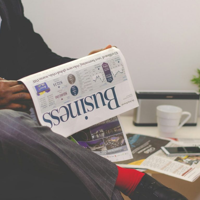Mann in Anzug hält eine Zeitung mit dem Titel "Business" in der Hand.