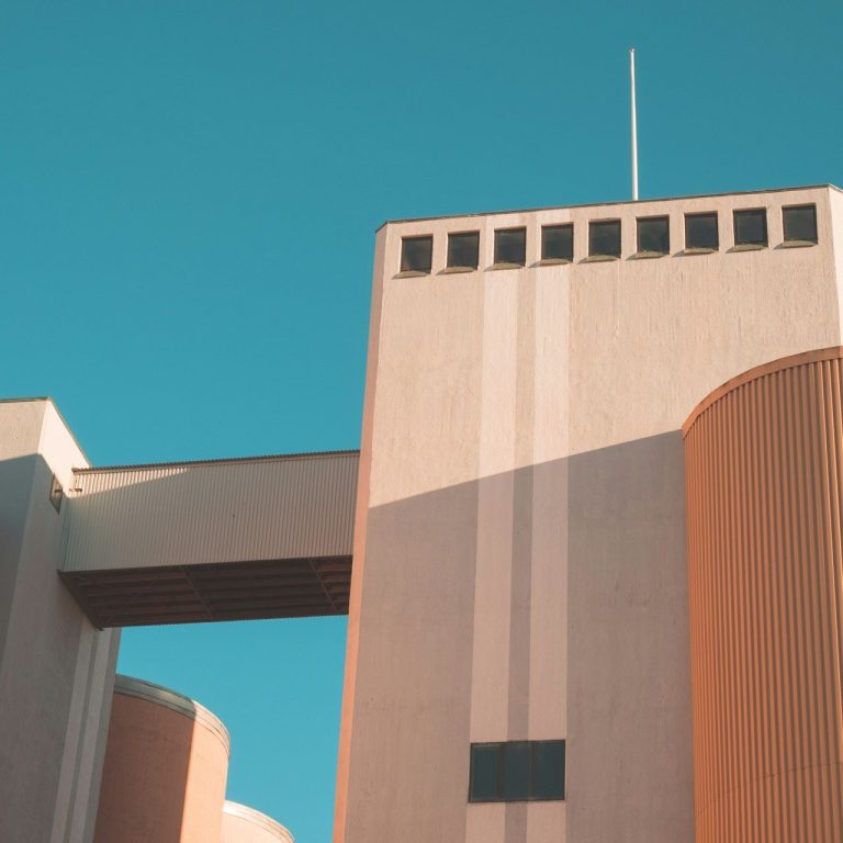 Moderne Architektur mit klaren Linien und orangenen sowie grauen Fassaden unter blauem Himmel.