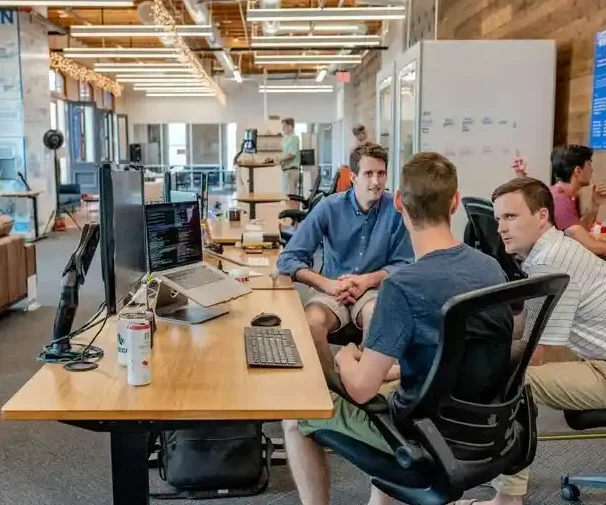 Drei Männer arbeiten in einem modernen Büro, diskutieren an einem Tisch mit Laptops.