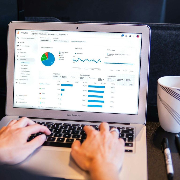 Person arbeitet an einem Laptop mit Diagrammen und Grafiken, neben einer Tasse.