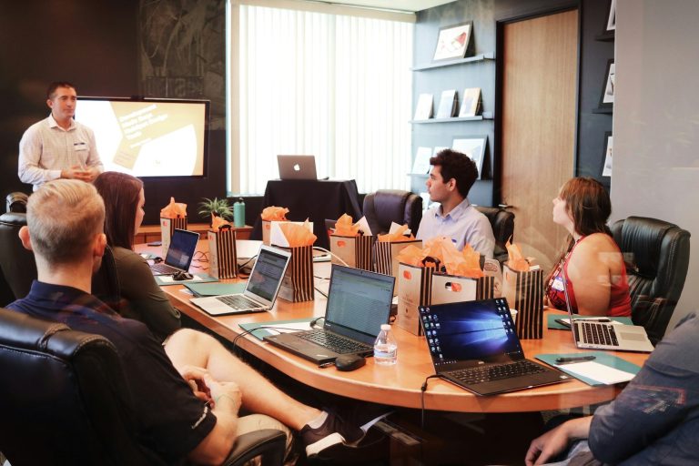 Männlicher Präsentierender vor einer Gruppe in einem Konferenzraum mit Laptops.